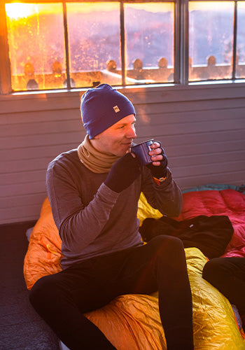 Person sitting in a beanbag chair with a mug, beside a window overlooking a scenic landscape.