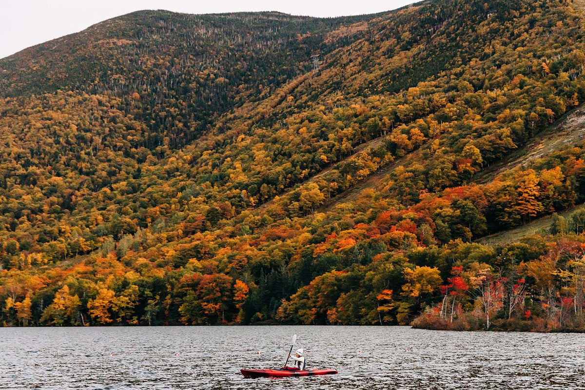 Someone kayaking in the fall with fall foliage behind them