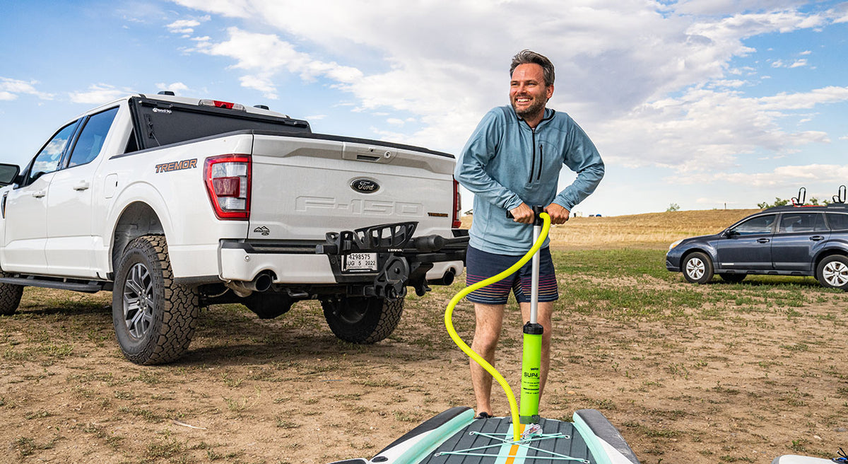 man pumping up paddle board wearing woolverino micro weight mid layer sun hoodie in color slate blue