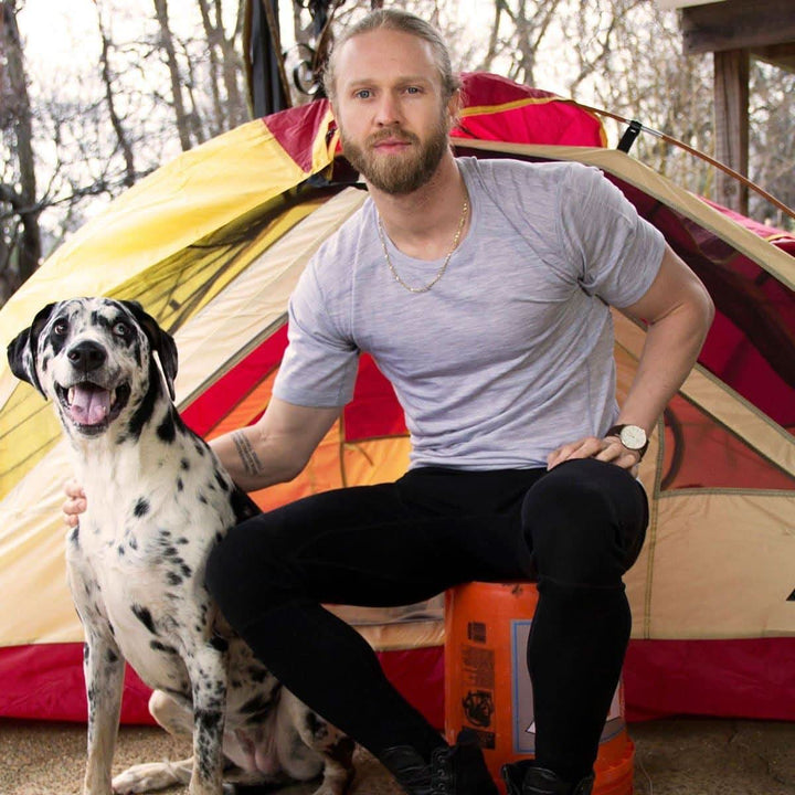 A man sits next to his Dalmatian in front of a tent modeling the microweight Merino wool t shirt, your perfect choice for hitting the gym or setting foot on the trails. Raglan sleeves and side panels create a garment that moves with you 
