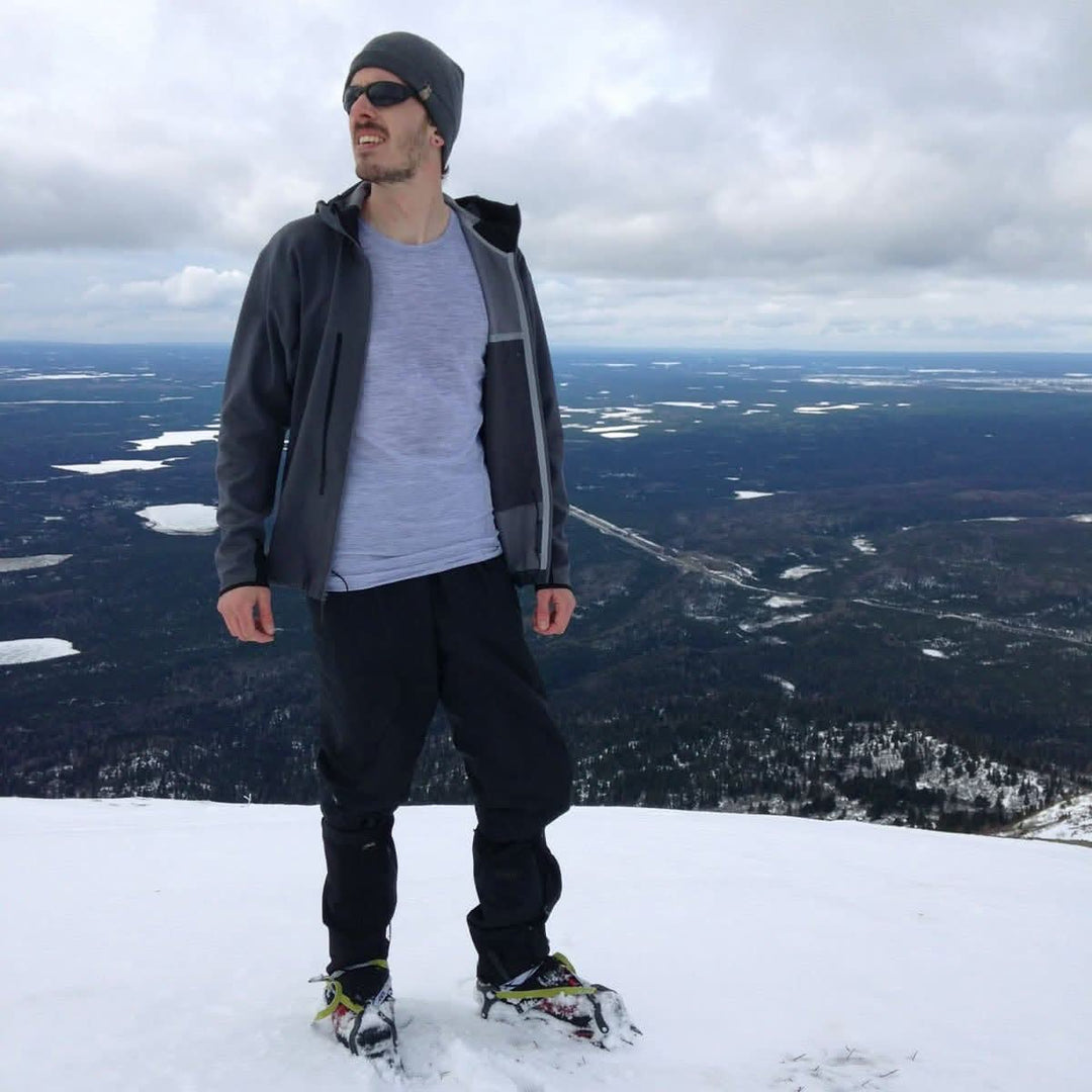 A man stands on a snowy summit in snowshoes. He wears the microweight Merino wool t shirt, the perfect first layer in any season! Raglan sleeves and side panels create a garment that moves with you 
