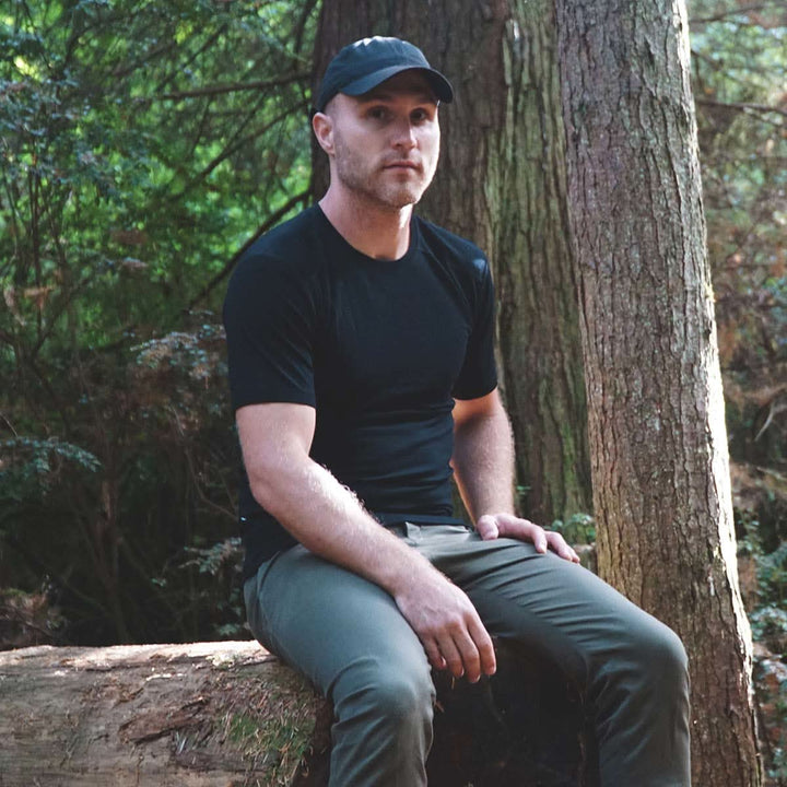 A man sits on a log modeling the microweight Merino wool t shirt, your perfect choice for hitting the gym or setting foot on the trails. Raglan sleeves and side panels create a garment that moves with you 