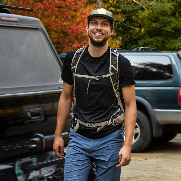 A man gets his backpack on and models the microweight Merino wool t shirt, your perfect choice for hitting the gym or setting foot on the trails. Raglan sleeves and side panels create a garment that moves with you 