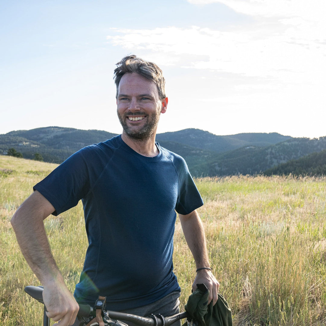 A man rides a bike in a field and models the microweight Merino wool t shirt, your perfect choice for hitting the gym or setting foot on the trails. Raglan sleeves and side panels create a garment that moves with you 