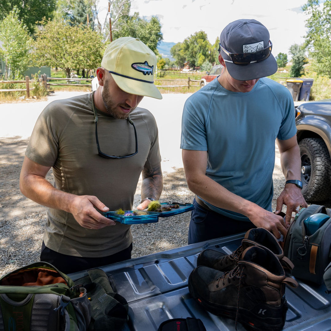 Two men prepare their fishing rods while wearing microweight merino wool t shirt with flat-brimmed hats and sunglasses. Raglan sleeves and side panels create a garment that moves with you 