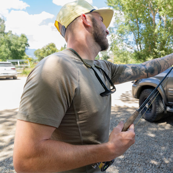 A man adjusts his fishing rod while wearing the microweight Merino wool t shirt, your perfect choice for hitting the gym or setting foot on the trails. Raglan sleeves and side panels create a garment that moves with you 