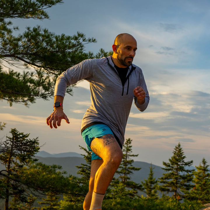 A man trail running in a microweight merino wool quarter zip sun hoodie.  