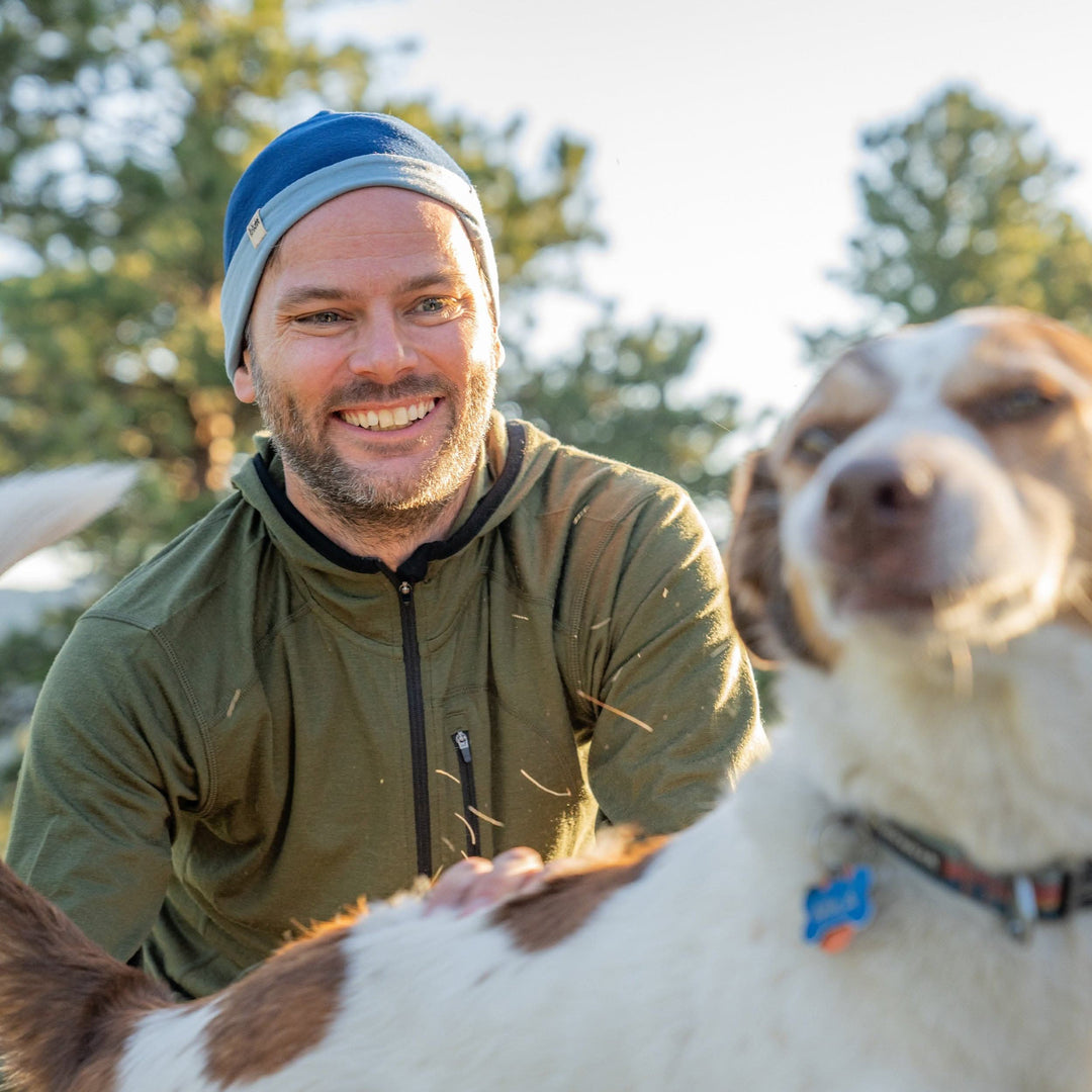 A man pets his dog while wearing the super light microweight merino wool quarter zip sun hoodie. 