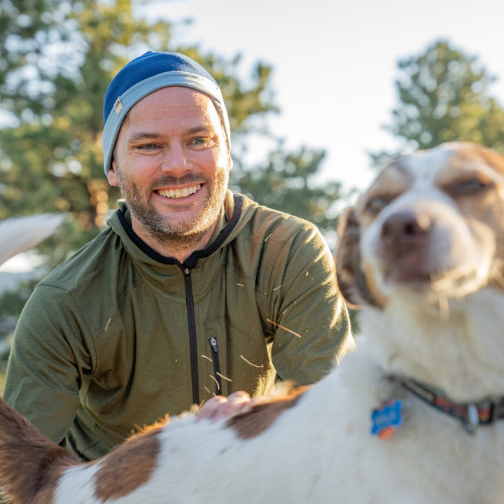 A man pets his dog while wearing the super light microweight merino wool quarter zip sun hoodie. 