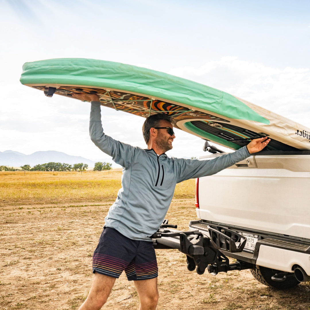 A man loads his paddleboard back into his truck while wearing the super light microweight merino wool quarter zip sun hoodie. 