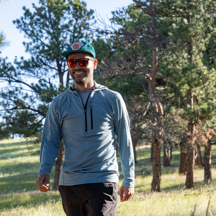 A man walks through a field wearing his super light microweight merino wool quarter zip sun hoodie.  