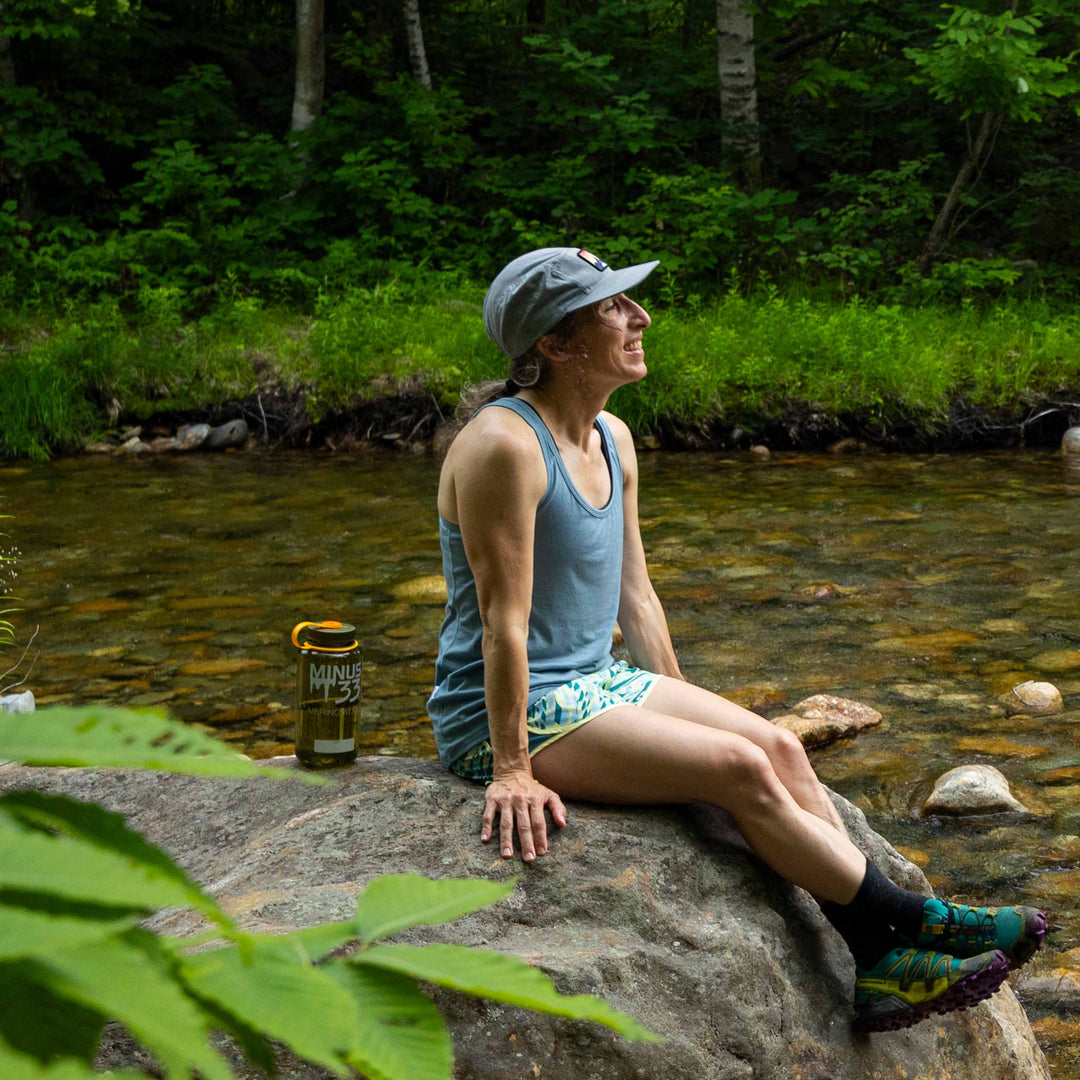 Womens microweight tank top super light merino wool for summer, woman sitting on a rock beside a stream 