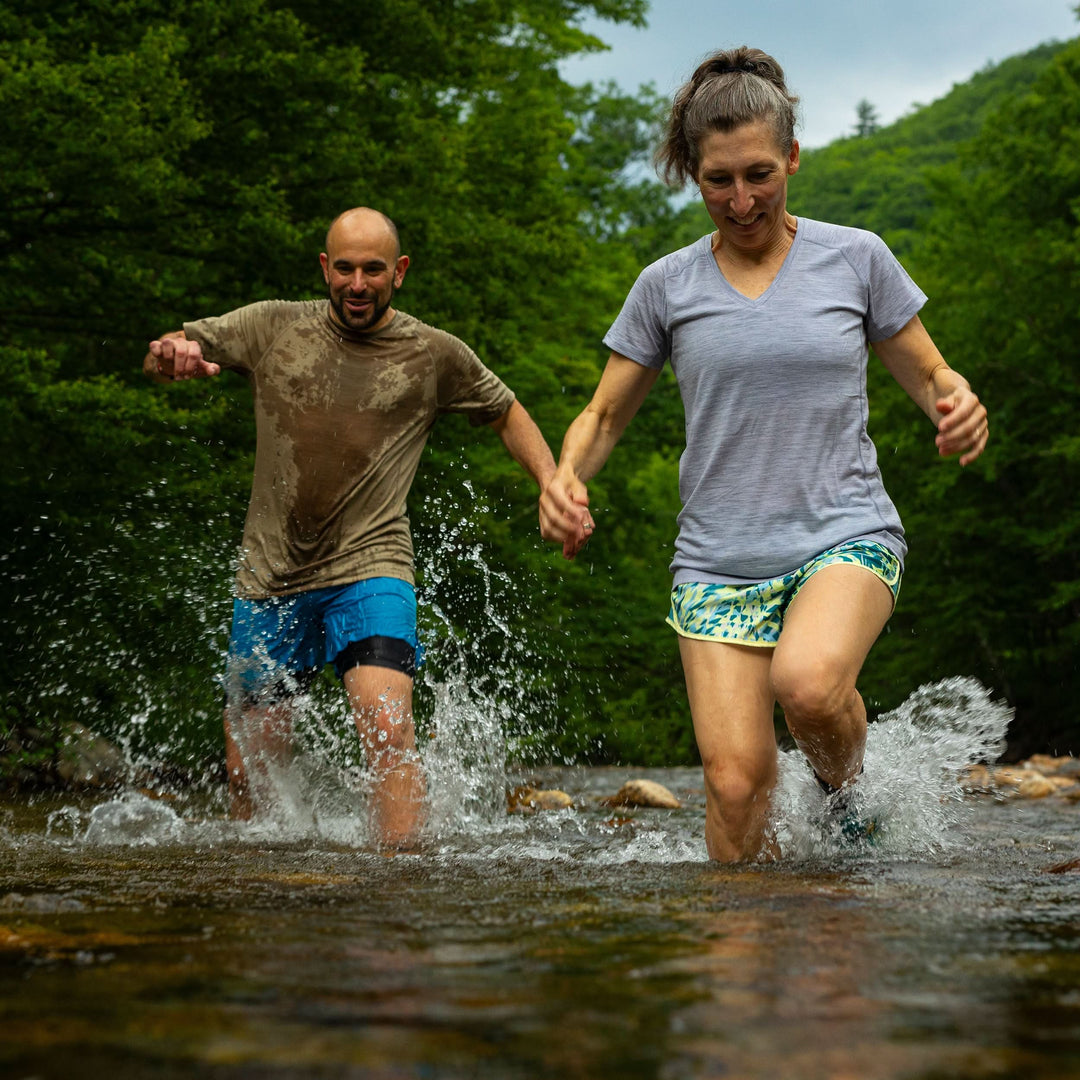 Woman wearing microweight merino wool v-neck runs through river 