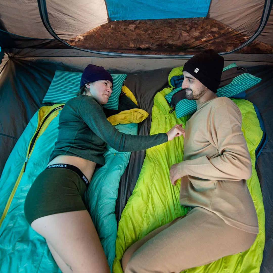 Two people lay on top of their sleeping bags facing each other. The woman models the microweight merino wool boyshorts. The boyshorts have a one inch inseam and a one inch woven sport elastic waistband 