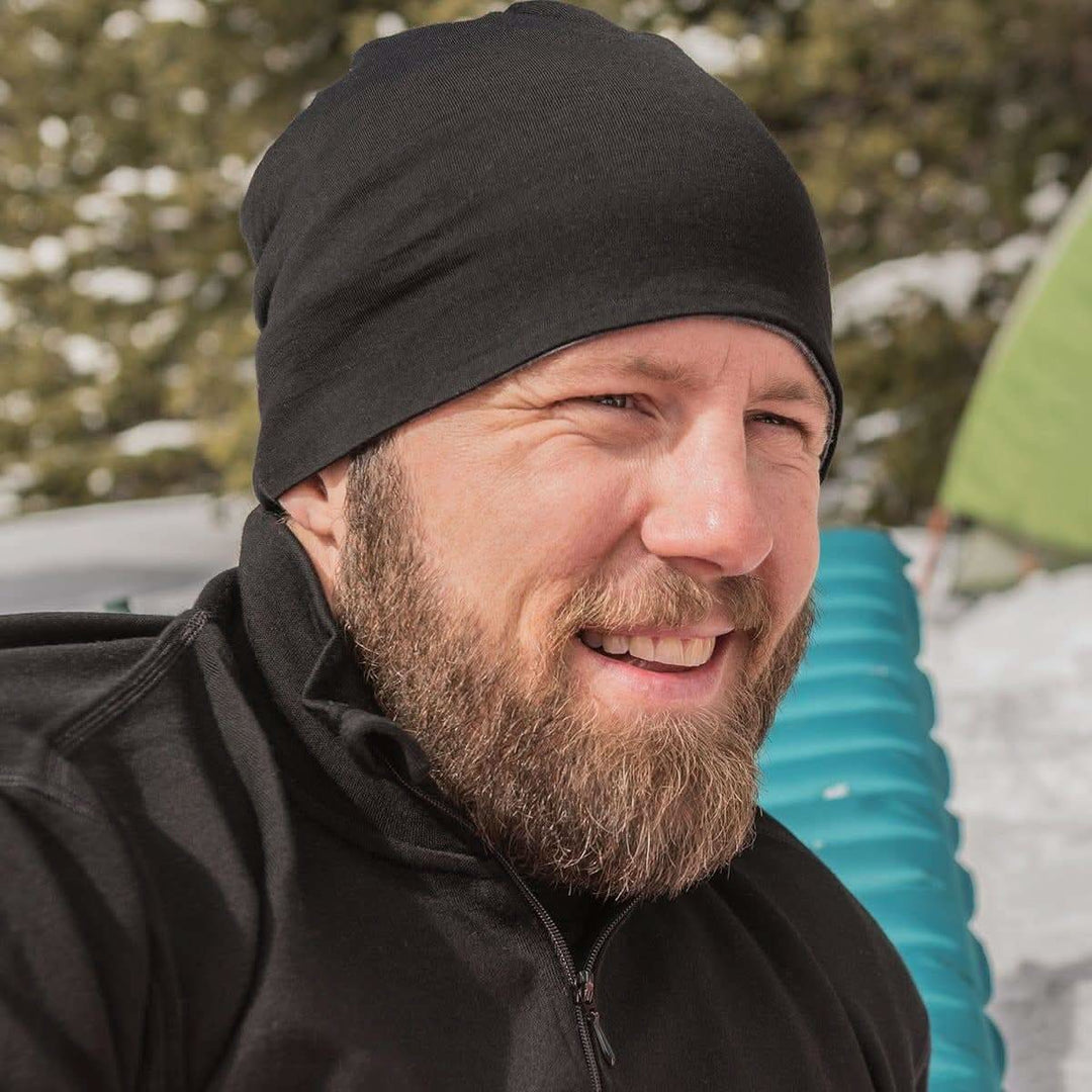 A man models the super lightweight reversible beanie. This merino wool blend beanie is slim enough to fit under a helmet, but warm enough to wear by itself on a chilly run, front three-quarter view outdoors 