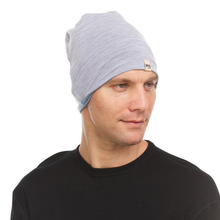 Side profile view of a male model wearing a slate blue and ash gray reversible merino wool blend beanie 