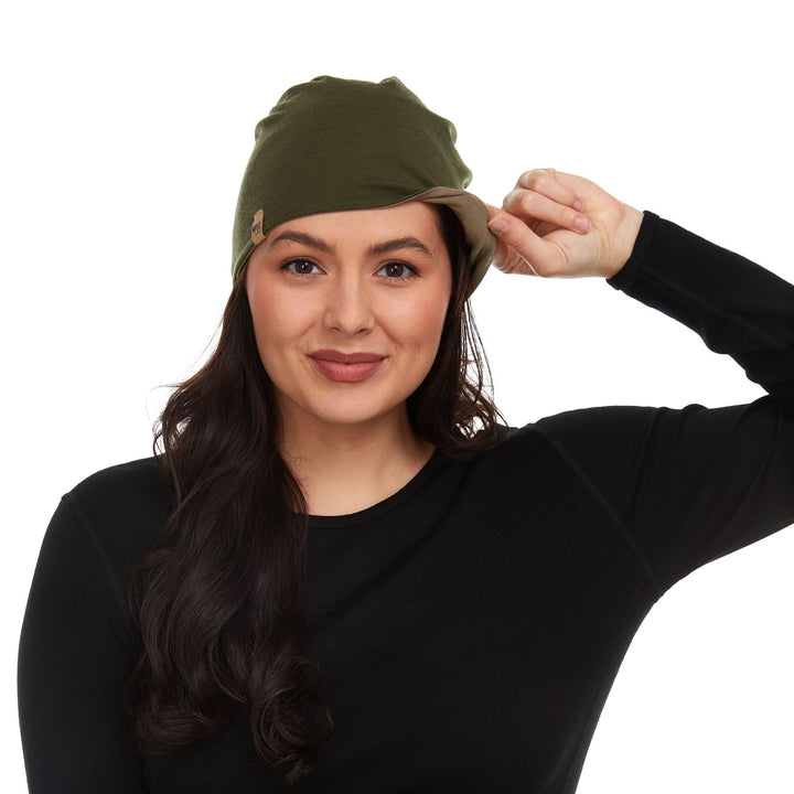 Side view of a male model wearing a tan and olive drab reversible merino wool blend beanie with the cuff flipped up 