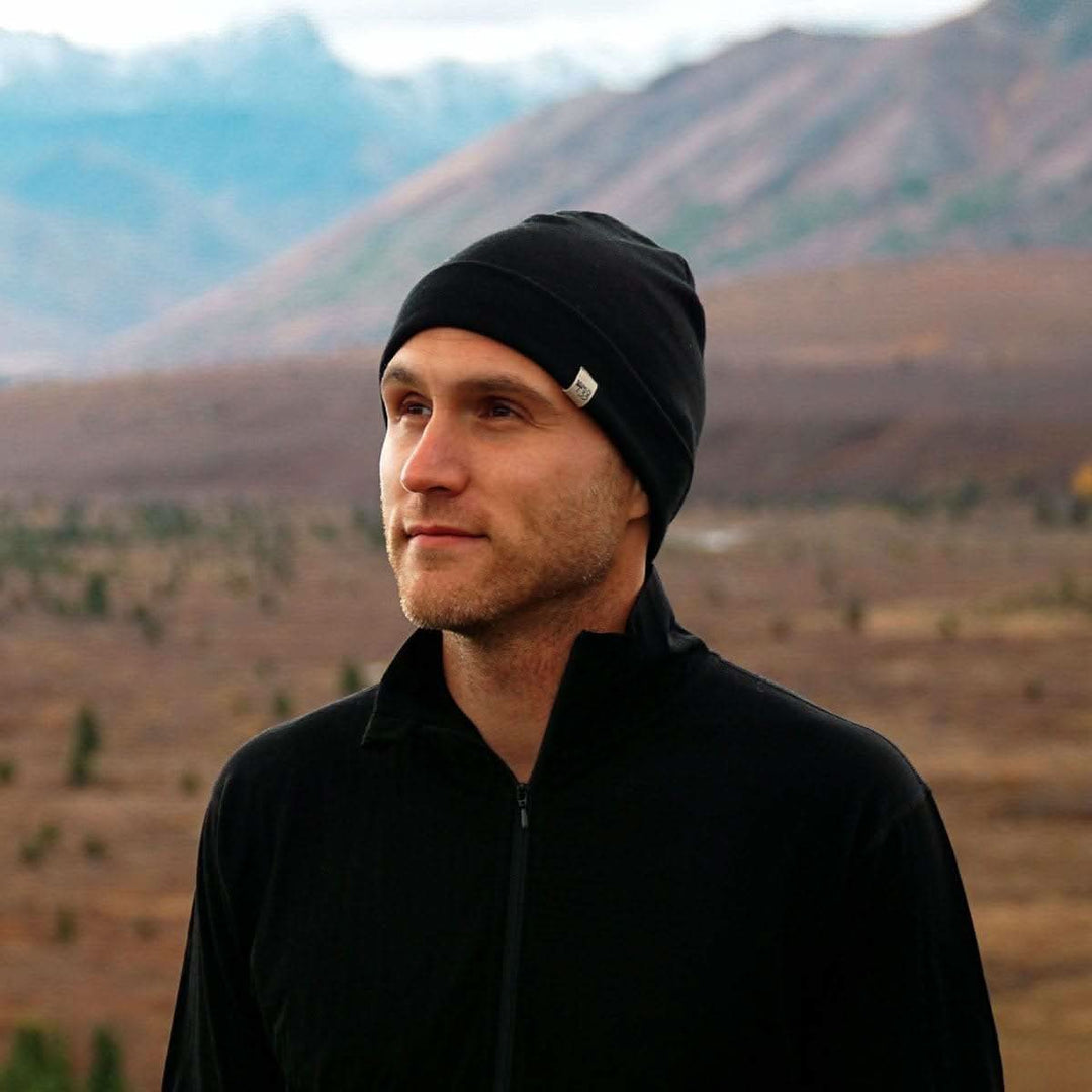 A man models the lightweight, double-layered, hundred percent, super soft merino wool beanie perfect for fall, winter, and spring. This hat is perfect for a hike up the mountain or a walk around the block, front three-quarter view outdoors 