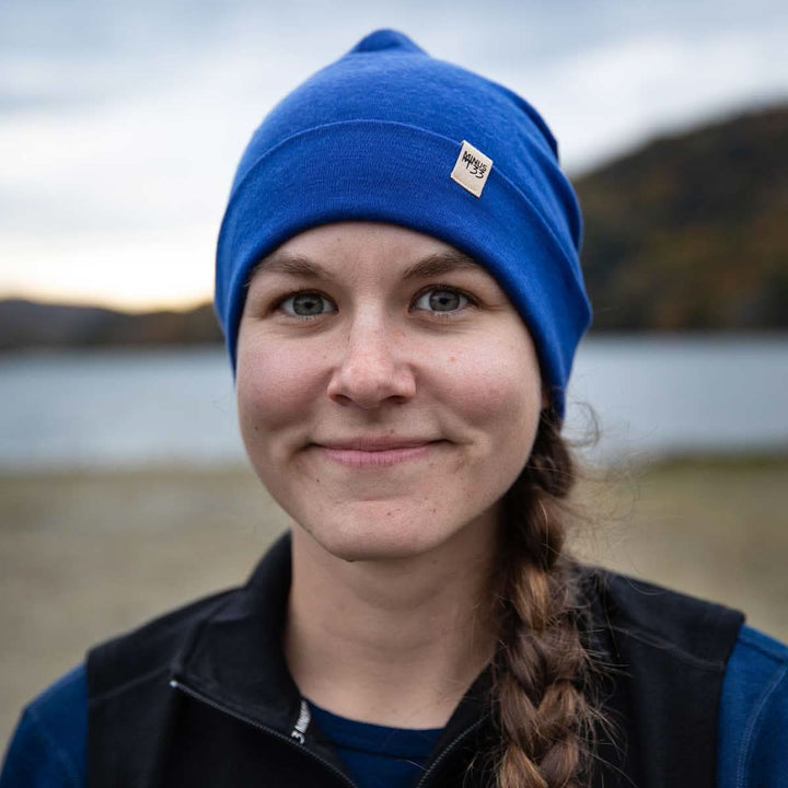 A woman models the lightweight, double-layered, hundred percent, super soft merino wool beanie perfect for fall, winter, and spring. This hat is perfect for a hike up the mountain or a walk around the block, front three-quarter view outdoors 