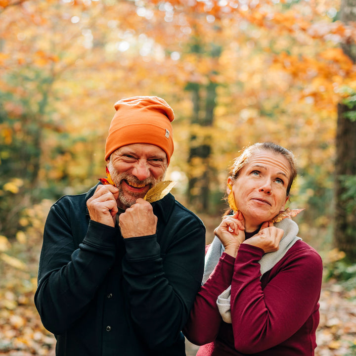 Two people get playful with leaves! A man models the lightweight, double-layered, hundred percent, super soft merino wool beanie perfect for fall, winter, and spring. This hat is perfect for a hike up the mountain or a walk around the block!
