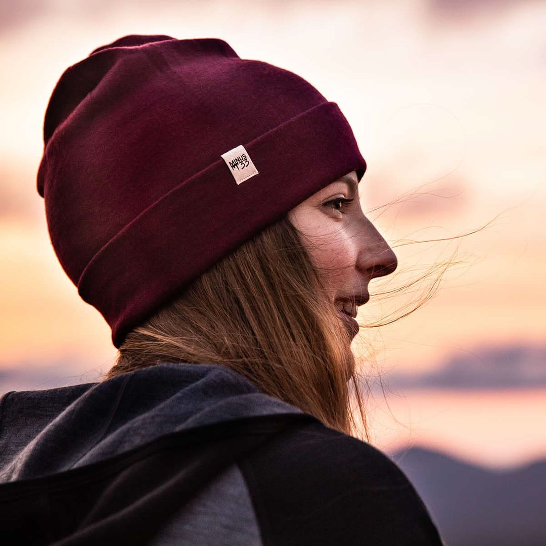 A woman watching the sunset models a lightweight, double-layered, hundred percent, super soft merino wool beanie with a midweight wool hoodie. This hat is perfect for a hike up the mountain or a walk around the block!
