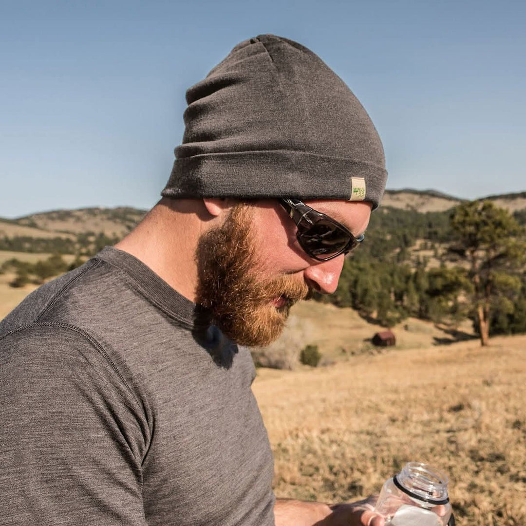 A man models the lightweight, double-layered, hundred percent, super soft merino wool beanie perfect for fall, winter, and spring. This hat is perfect for a hike up the mountain or a walk around the block, front three-quarter view outdoors 