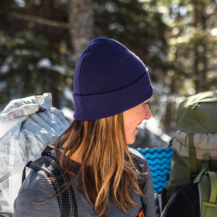 A woman models a lightweight, double-layered, hundred percent, super soft merino wool beanie perfect for fall, winter, and spring. This hat is perfect for a hike up the mountain or a walk around the block, front view on a hiking trail 