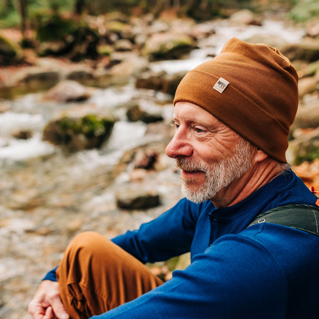 A man models a lightweight, double-layered, hundred percent, super soft merino wool beanie with a midweight long sleeve henley top. This hat is perfect for a hike up the mountain or a walk around the block!
