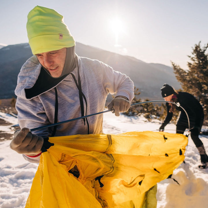 A man setting up a tent models a lightweight, double-layered, hundred percent, super soft merino wool beanie perfect for fall, winter, and spring. This hat is perfect for a hike up the mountain or a walk around the block!
