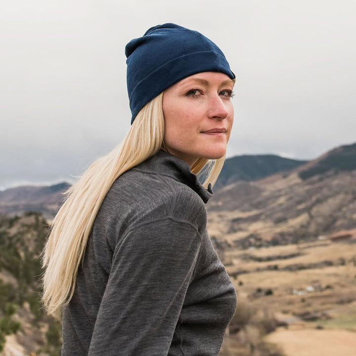 A woman models the lightweight, double-layered, hundred percent, super soft merino wool beanie perfect for fall, winter, and spring. This hat is perfect for a hike up the mountain or a walk around the block, front three-quarter view outdoors 
