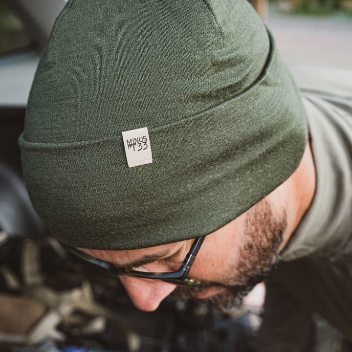 A man models the lightweight, double-layered, hundred percent, super soft merino wool beanie perfect for fall, winter, and spring. This hat is perfect for a hike up the mountain or a walk around the block, front three-quarter view outdoors 