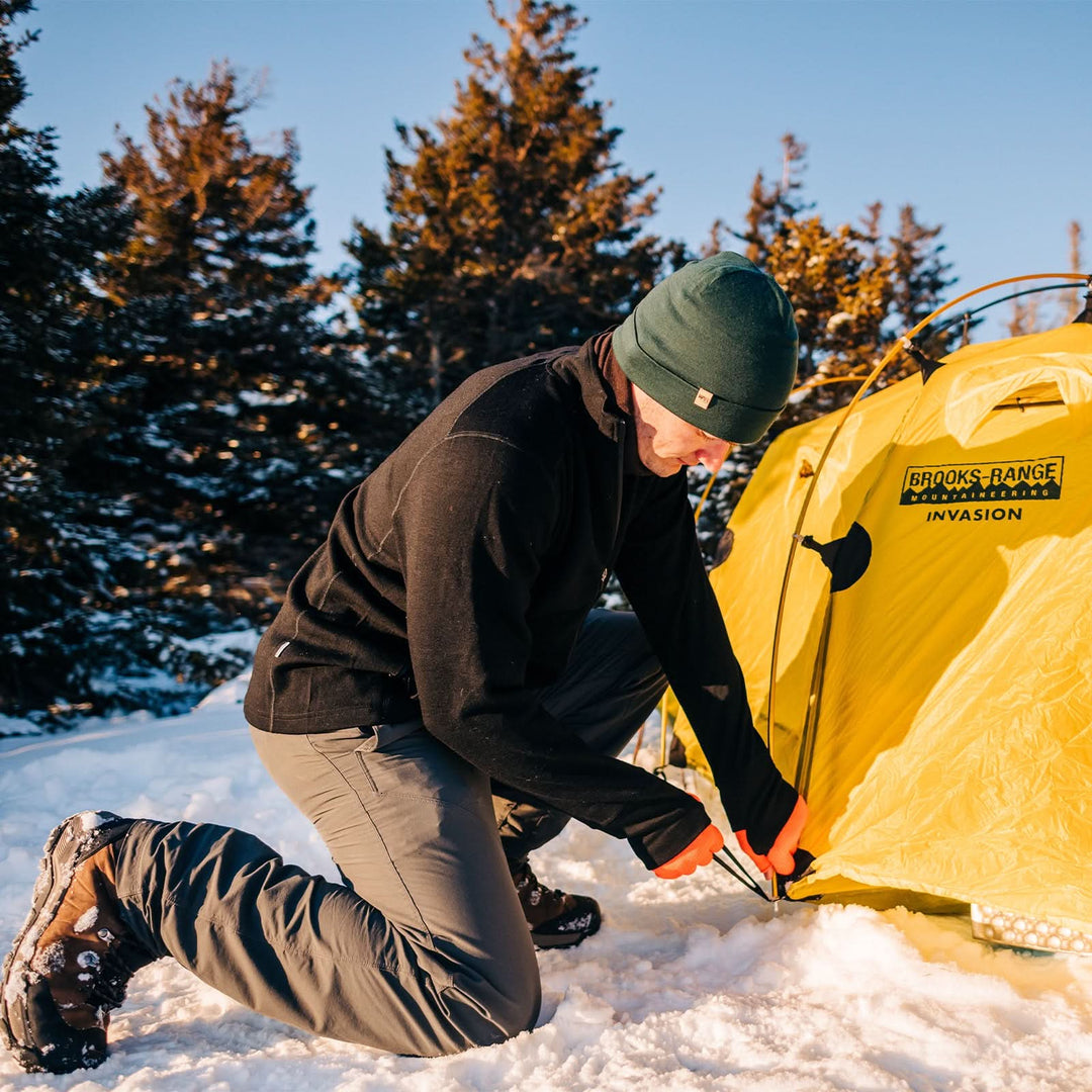 A man wears the lightweight, double-layered, hundred percent, super soft merino wool beanie while setting up his tent. This hat is perfect for a hike up the mountain or a walk around the block!
