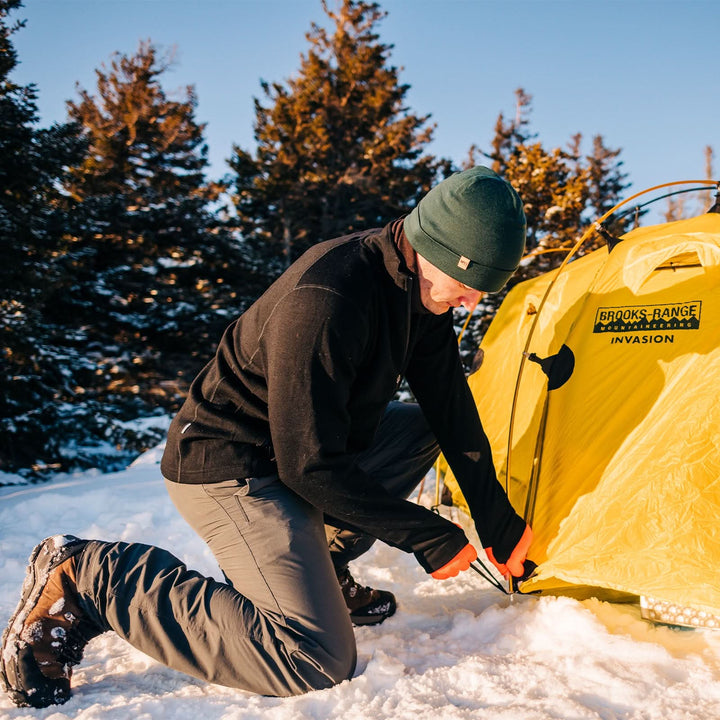 A man wears the lightweight, double-layered, hundred percent, super soft merino wool beanie while setting up his tent. This hat is perfect for a hike up the mountain or a walk around the block!
