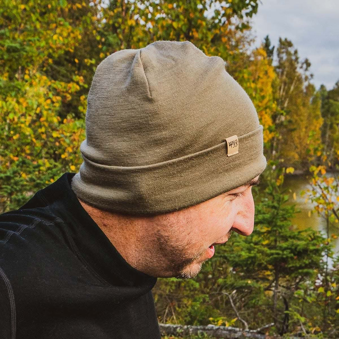 A man models the lightweight, double-layered, hundred percent, super soft merino wool beanie perfect for fall, winter, and spring. This hat is perfect for a hike up the mountain or a walk around the block, front three-quarter view outdoors 