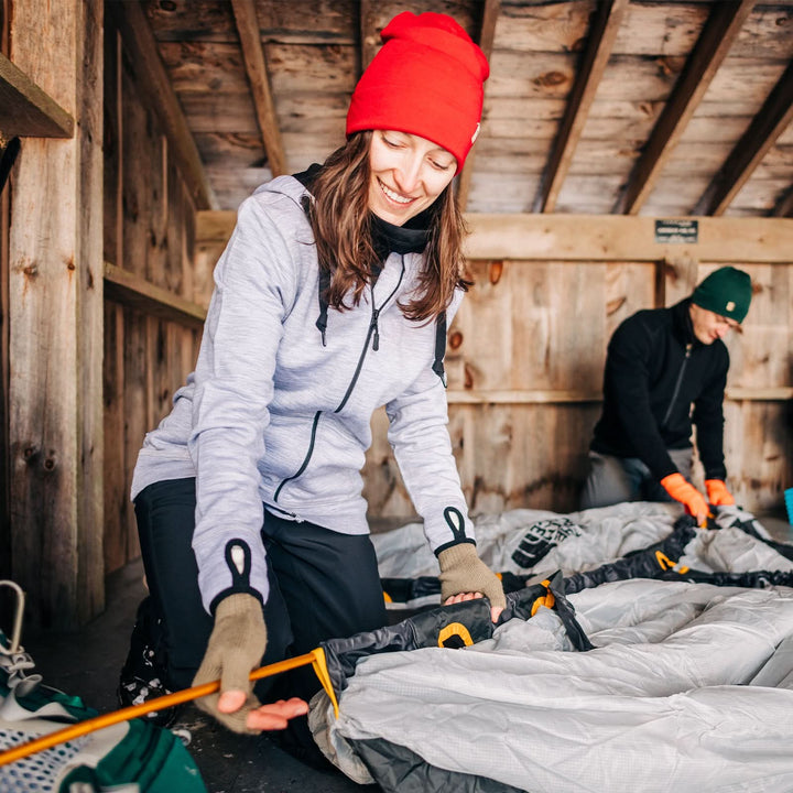 A woman setting up a tent models a lightweight, double-layered, hundred percent, super soft merino wool beanie perfect for fall, winter, and spring. This hat is perfect for a hike up the mountain or a walk around the block!
