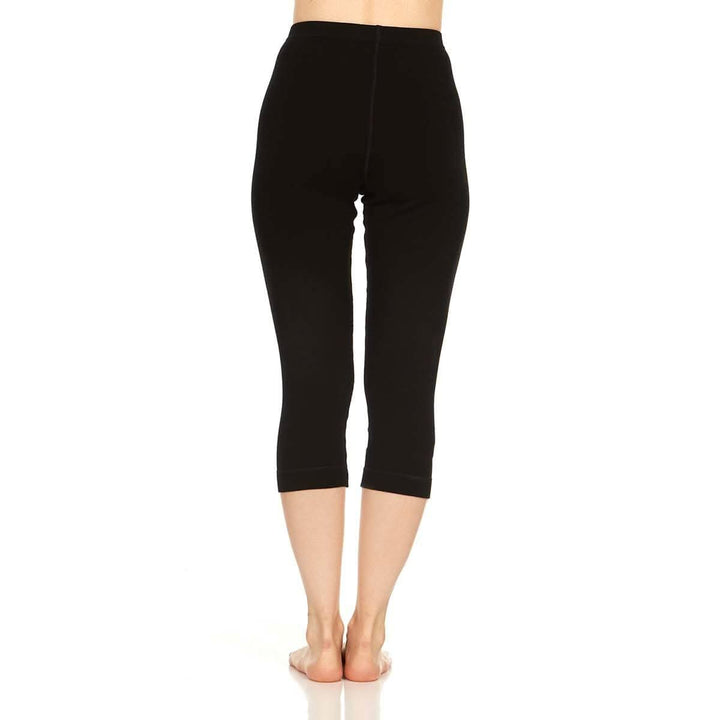 Back full-length view from waist to feet of a woman wearing black Osceola midweight merino wool three-quarter base-layer bottoms, showing the high waistband, centered rear seam, close-fitting legs, and even mid-calf cuffs