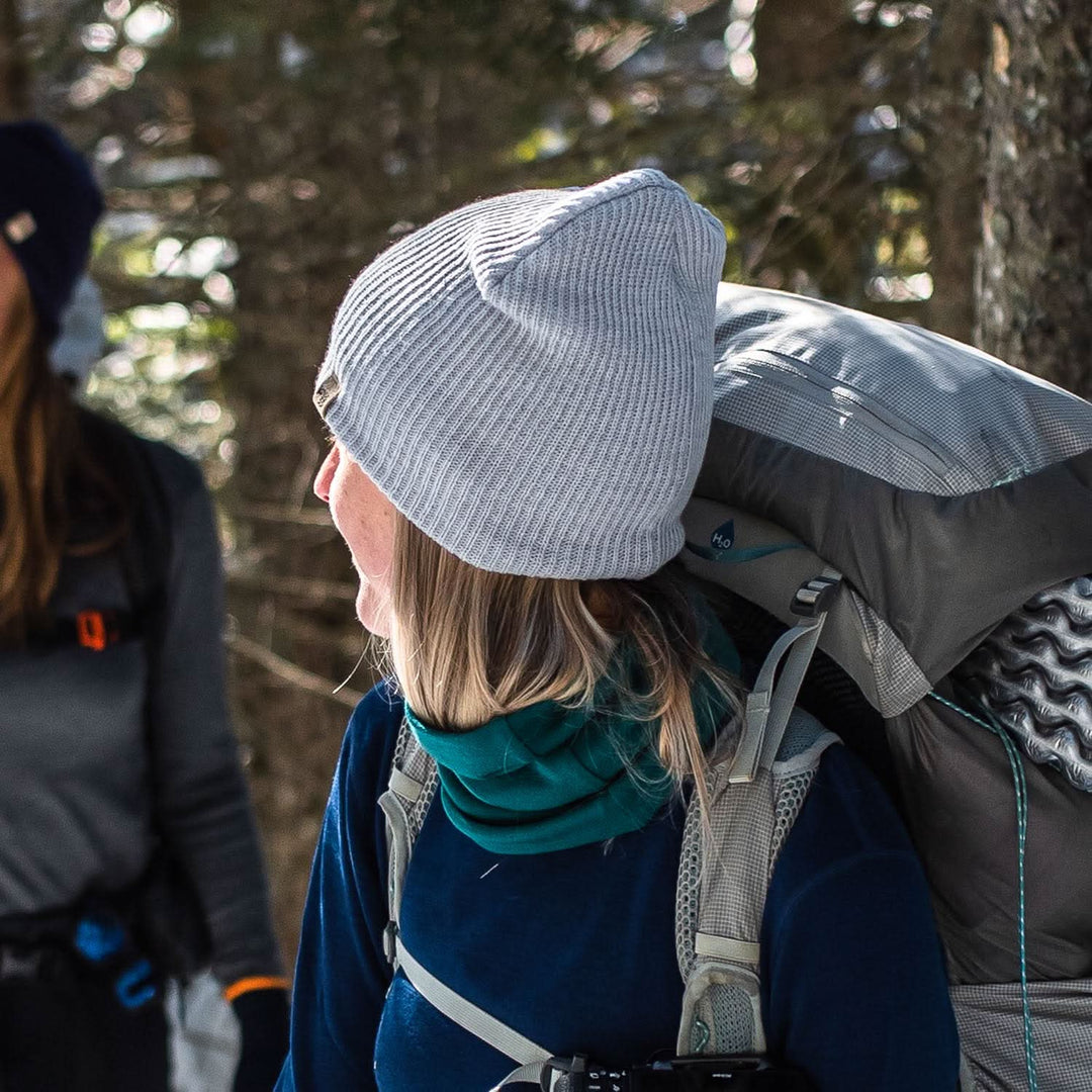 A woman looks back at her hiking partner while wearing the midweight hundred percent merino wool beanie 