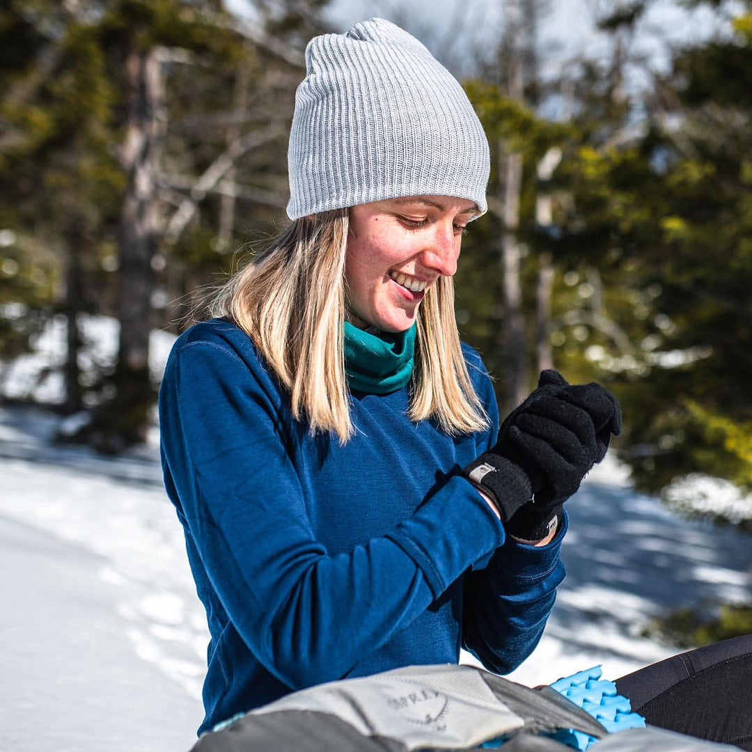 A woman warms up in the sunlight modeling the midweight hundred percent merino wool beanie 