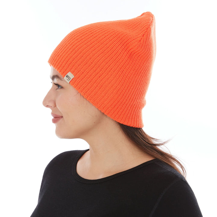 Side profile view of a female model wearing a blaze orange midweight 100% merino wool beanie with a folded cuff 