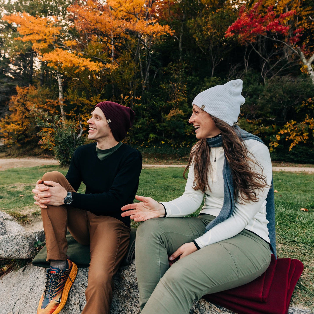 A woman sits outdoors to model the midweight hundred percent merino wool beanie 