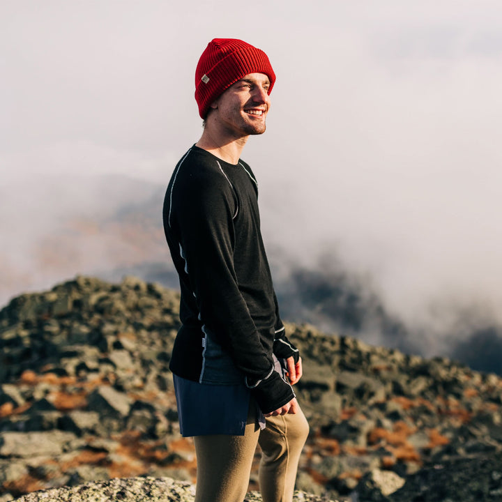 A man on the mountaintop models the midweight hundred percent merino wool beanie 
