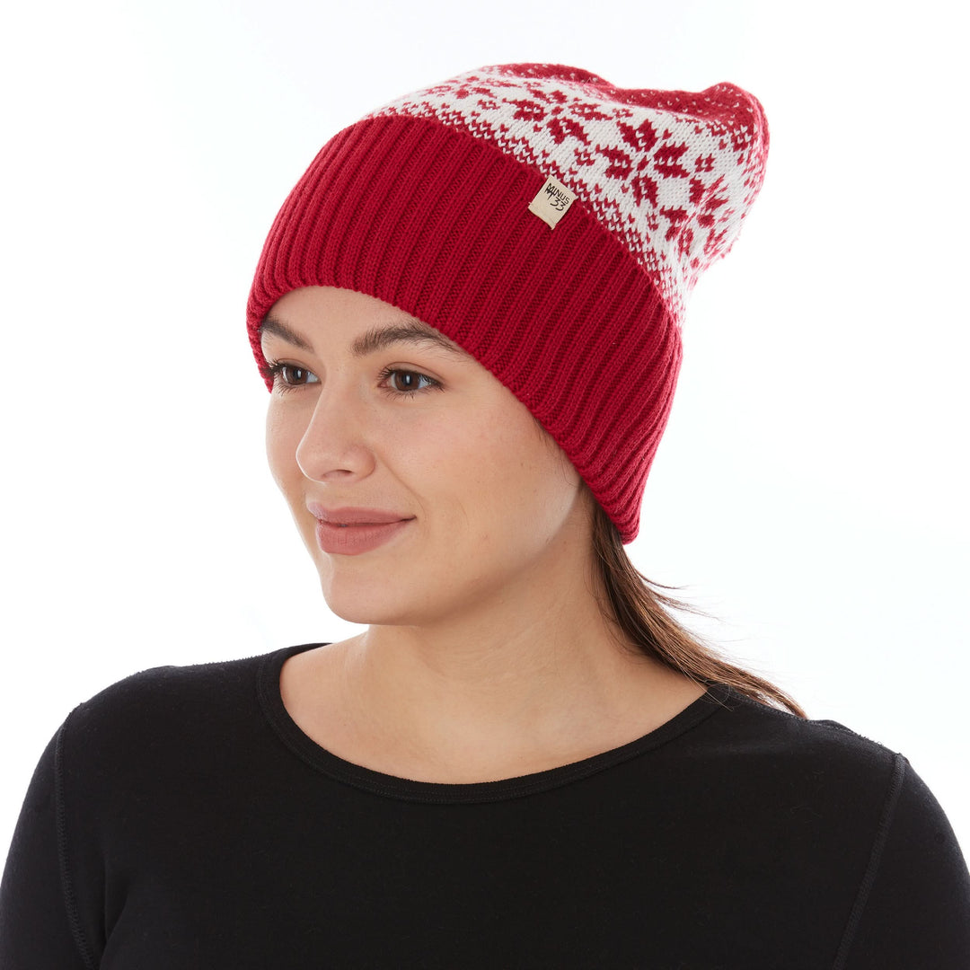Close-up front left three-quarter view of a woman wearing a true red midweight merino wool cuffed beanie with a natural cream snowflake-patterned crown and a small Minus33 logo patch 