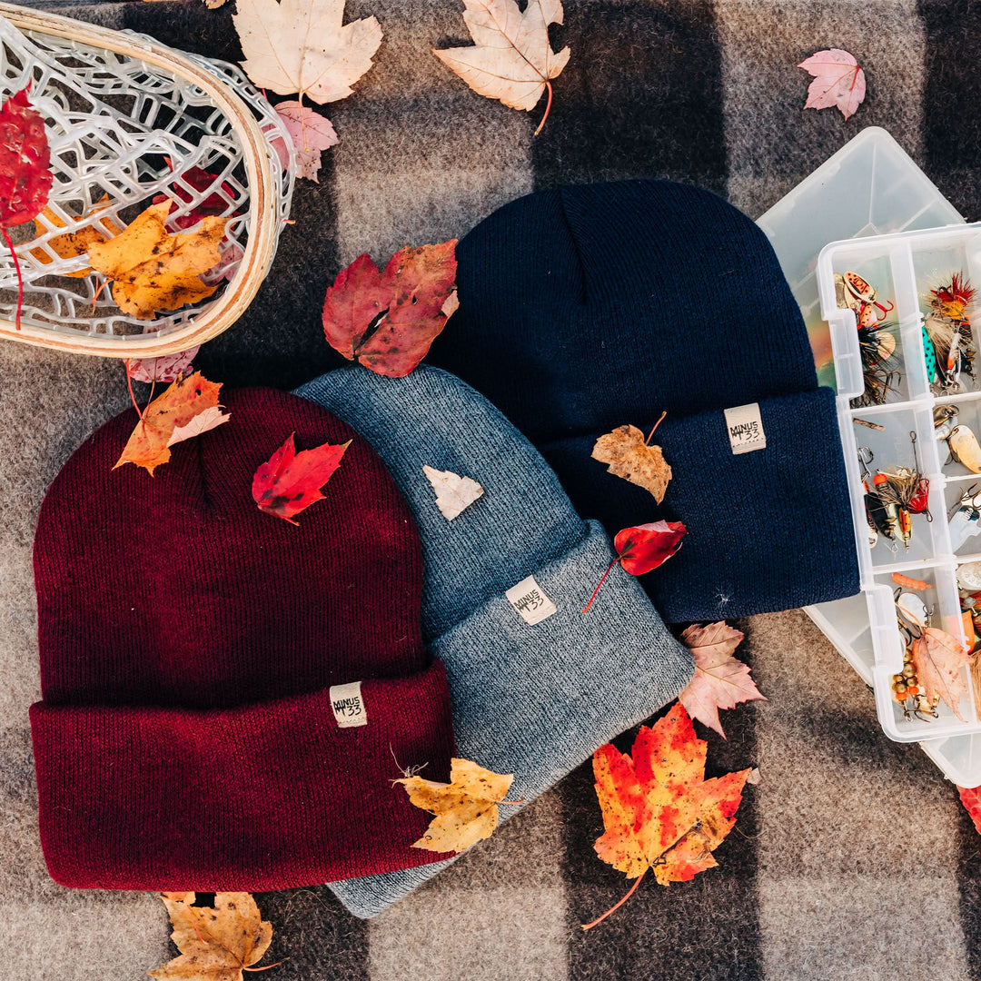 Three midweight hats sit between a tacklebox and a basket, on top of a Minus33 recycled wool blanket. 