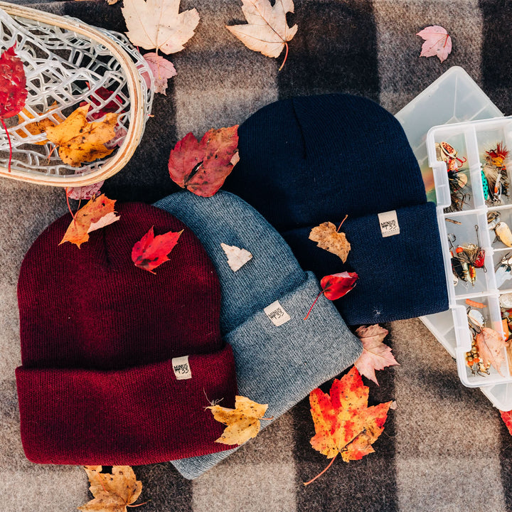 Three midweight hats sit between a tacklebox and a basket, on top of a Minus33 recycled wool blanket. 
