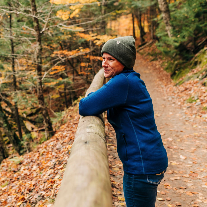 A woman on an autumn trail models the midweight, double-layered, hundred percent, super soft merino wool beanie that keeps you warm, but won&