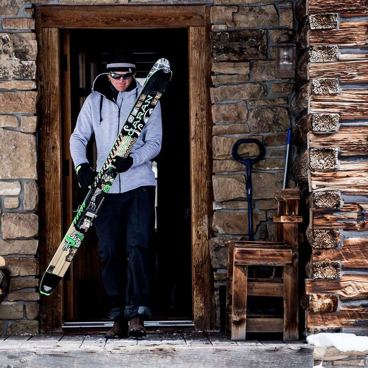 A man comes out of a cabin with skis in hand. The man is modeling the heavyweight brushed wool Kodiak Fleece Hoodie, crafted with thumbholes and a drawstring to bundle you up for wicked cold days! 