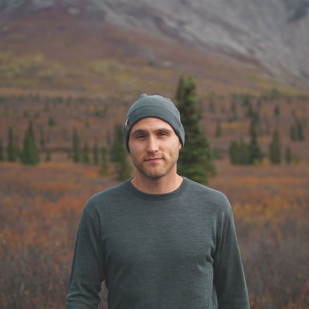 A man models a super soft, long sleeved merino wool thermal base layer crew. This top makes for a perfect first layer on a winter hike, or a nice casual wear on the chilly days of autumn and spring, front three-quarter view outdoors 