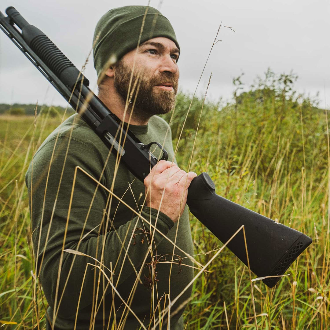 A man models a super soft, long sleeved merino wool thermal base layer crew. This top makes for a perfect first layer on a winter hike, or a nice casual wear on the chilly days of autumn and spring, front view in a grassy field 