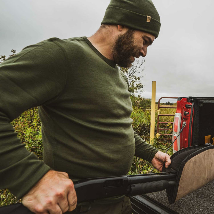 A man models a super soft, long sleeved merino wool thermal base layer crew. This top makes for a perfect first layer on a winter hike, or a nice casual wear on the chilly days of autumn and spring, front view carrying a backpack 