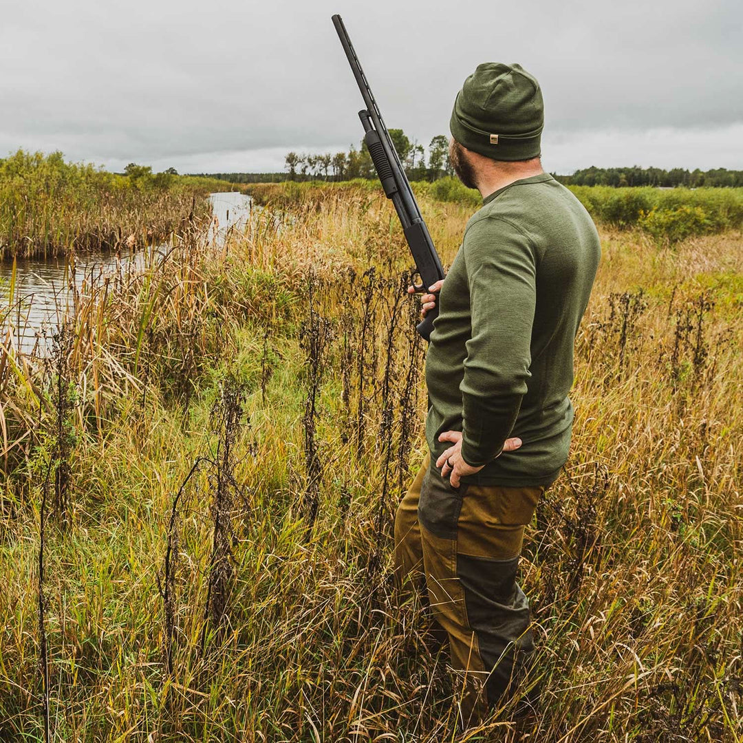 A man models a super soft, long sleeved merino wool thermal base layer crew. This top makes for a perfect first layer on a winter hike, or a nice casual wear on the chilly days of autumn and spring, front view beside the water 